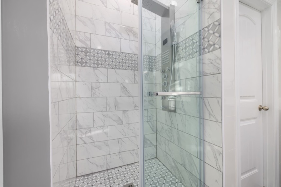 A person's hand points to a section of crumbling grout in a tiled shower wall.