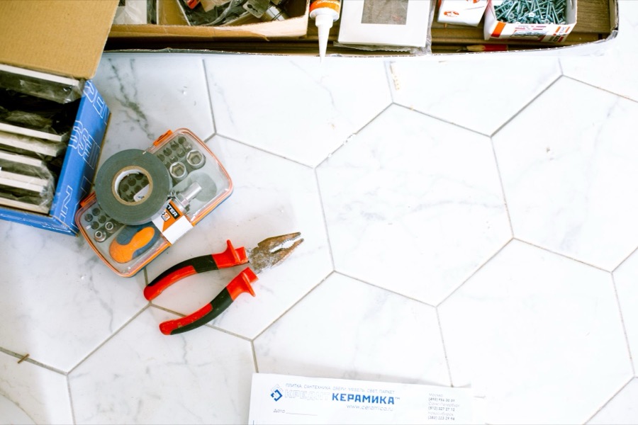 Various tools and materials for regrouting a shower, including a grout saw, new grout mix, and a float.