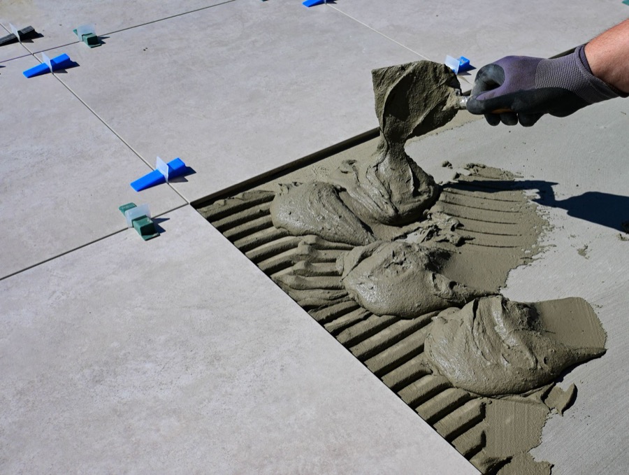 Close-up of a hand using a grout removal tool to carefully scrape out old, damaged grout from between tiles.