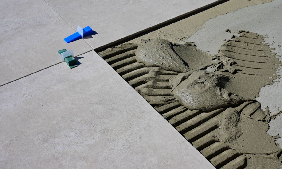 Close-up of a person using a specialized tool to carefully remove old, cracked grout from between white ceramic tiles.