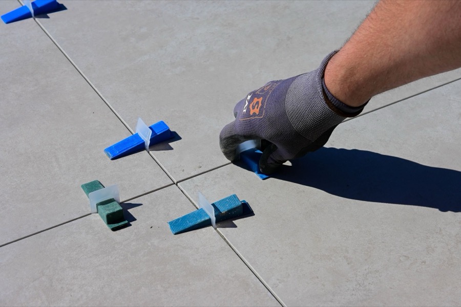 A worker's hand uses a rubber grout float to press fresh gray grout into the spaces between newly installed white subway tiles.