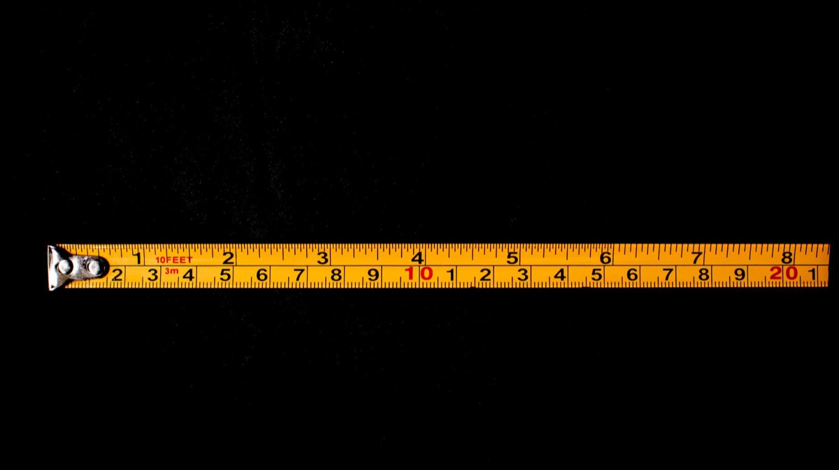 Close-up of a level tool or straight edge revealing lippage (uneven height) between two installed ceramic floor tiles.