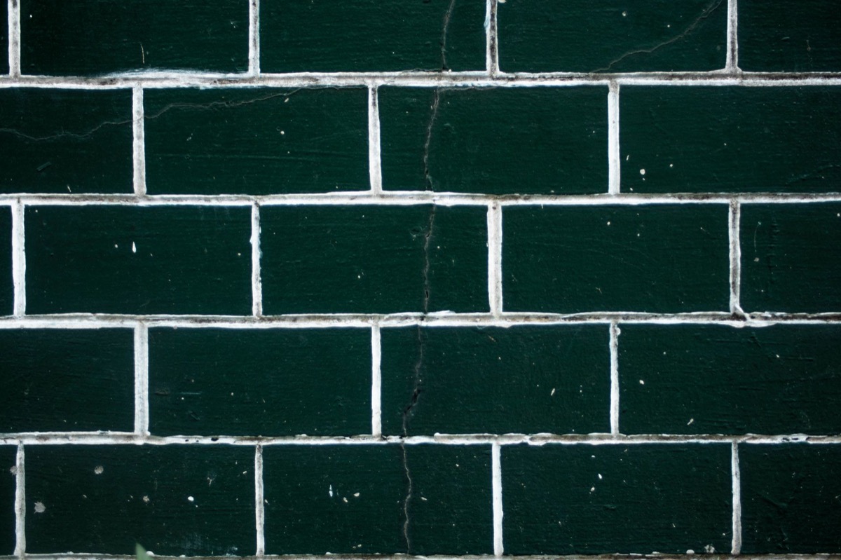 Close-up of severely cracked and discolored grout lines in a tiled shower wall, indicating water damage.